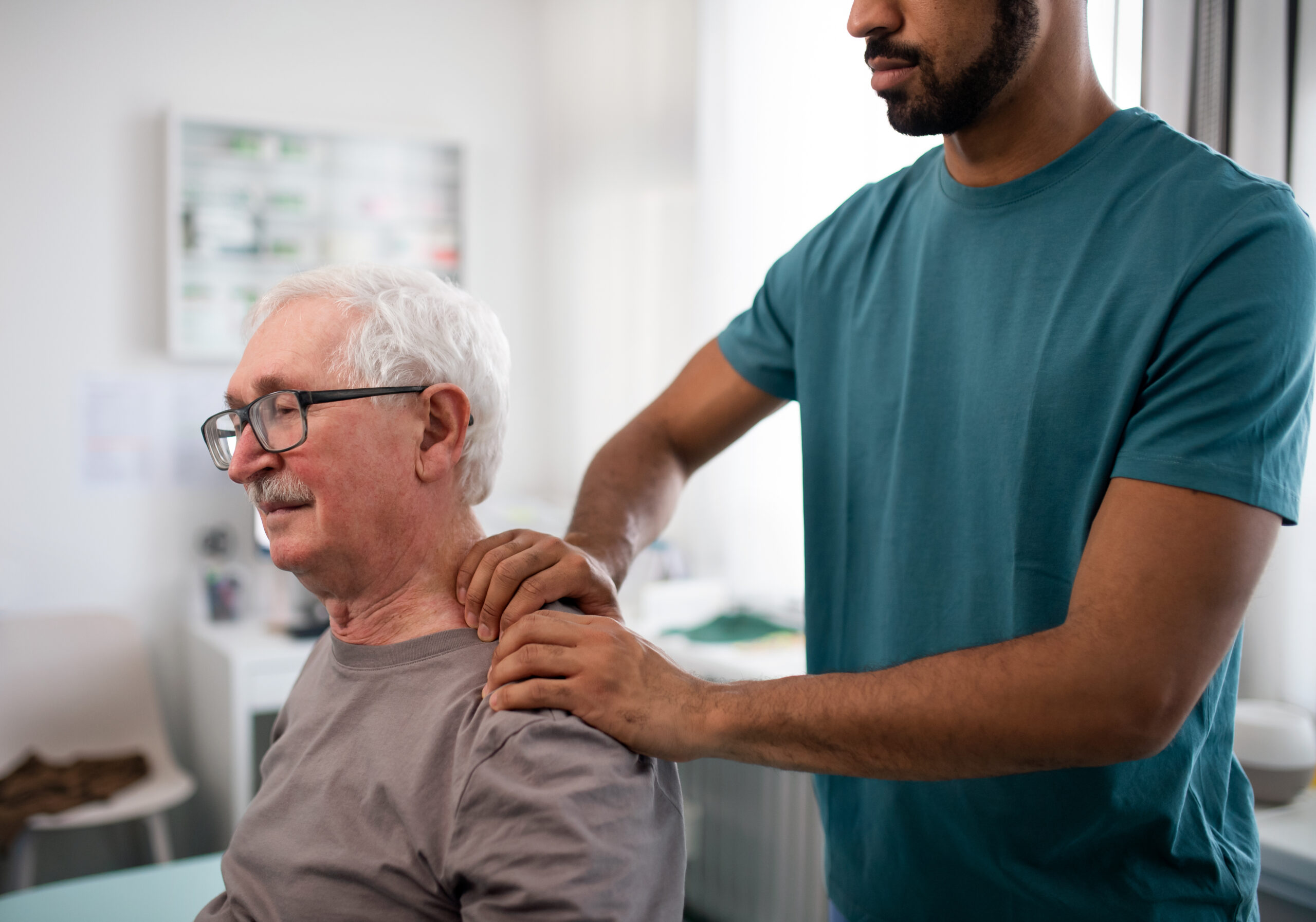 Young physiotherapist massaging the neck of senior patient in a physic room